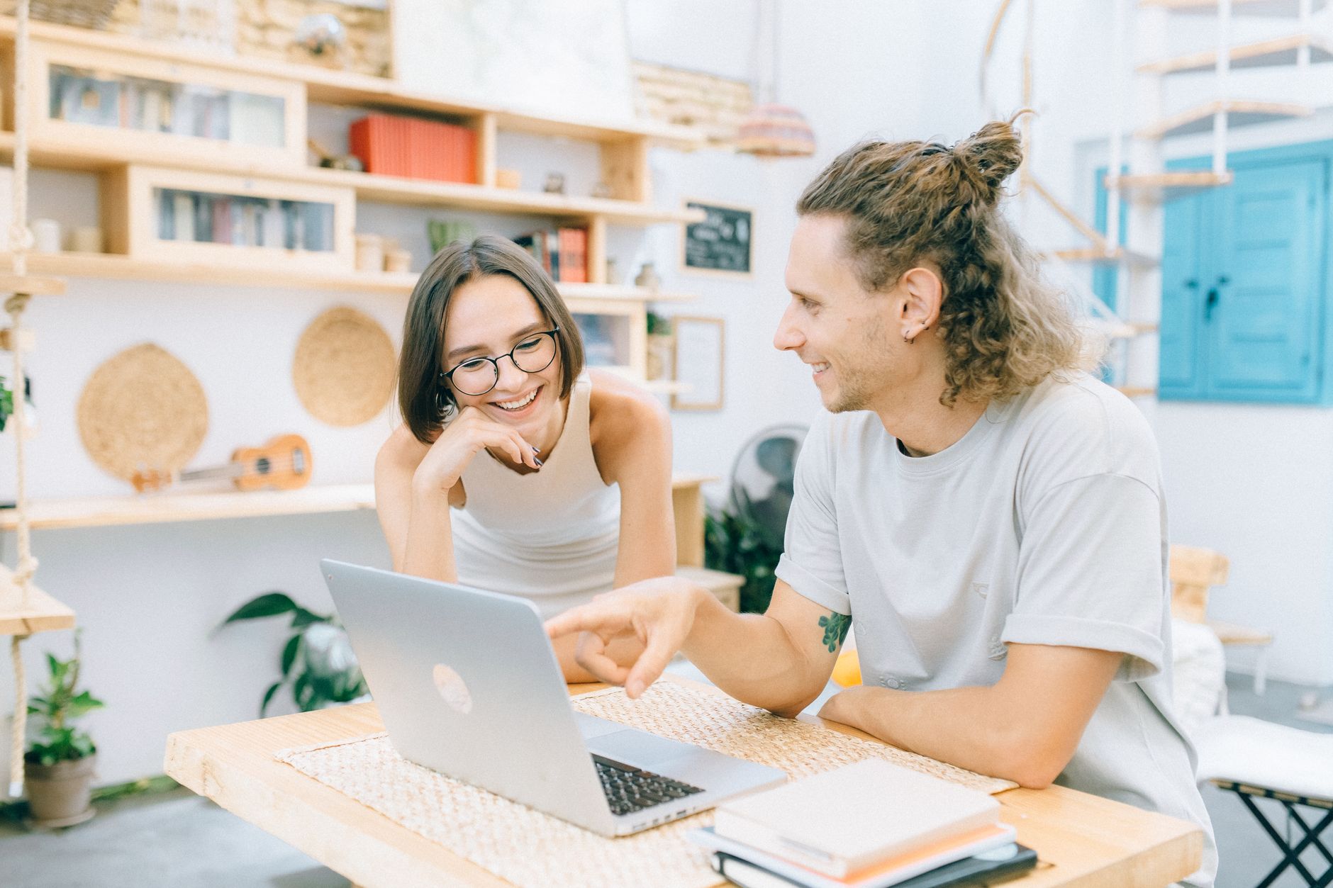 Two colleagues share a smile while discussing a project on a laptop in a cozy workspace.