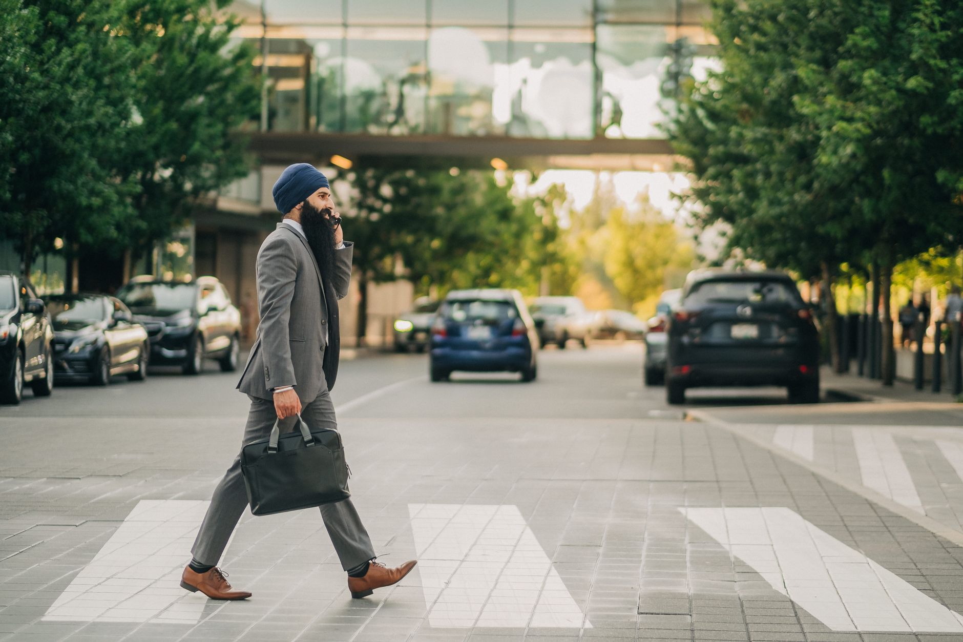 Sikh businessman with a turban crossing a city street on a zebra crossing, carrying a briefcase.